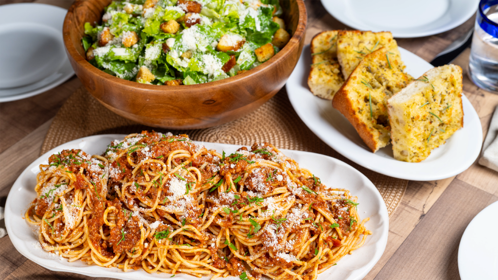 Spaghetti with meat sauce, Caesar salad and garlic bread on a table.