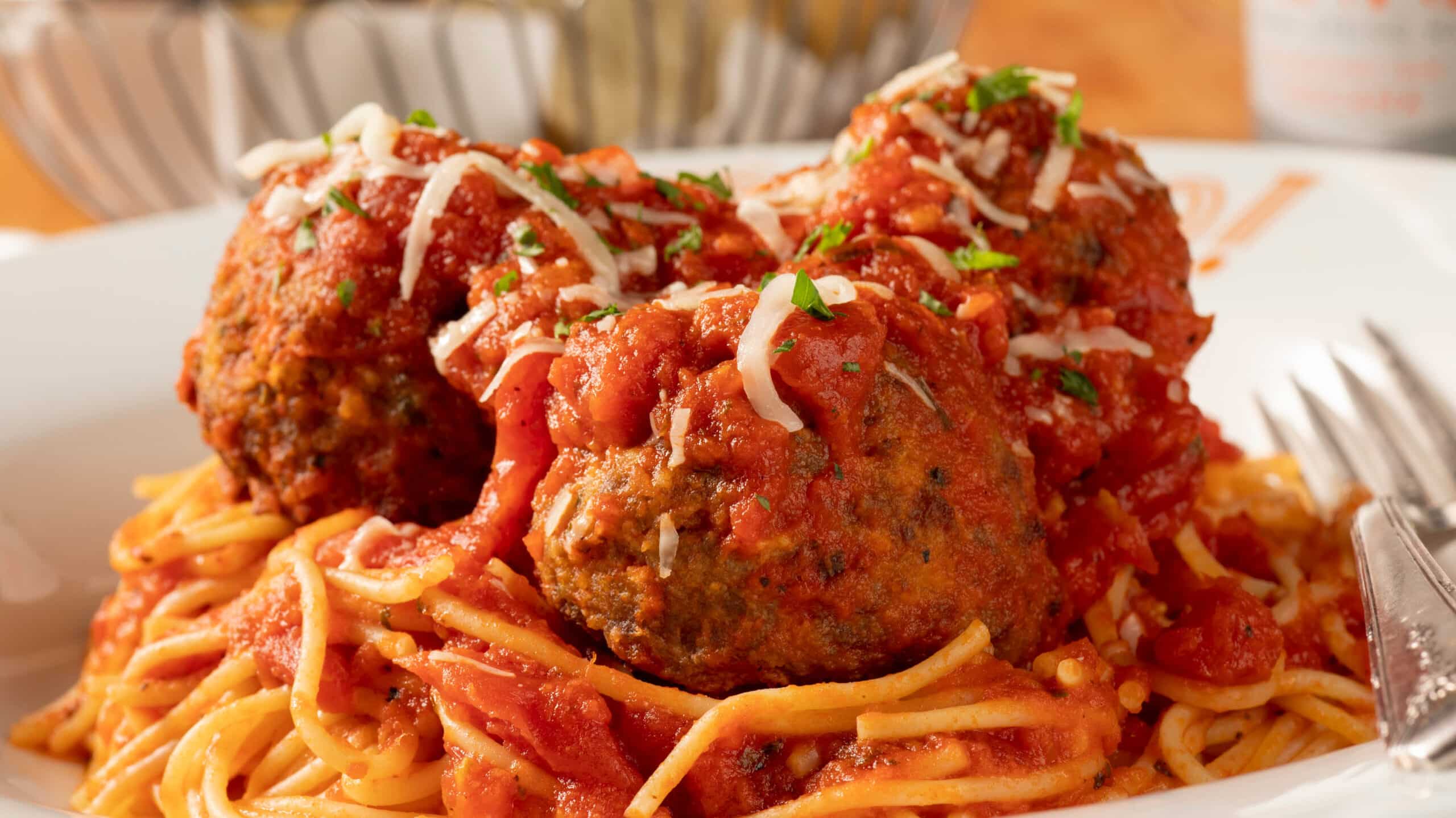 Three meatballs covered in sauce and cheese plated on top of Bravo's spaghetti