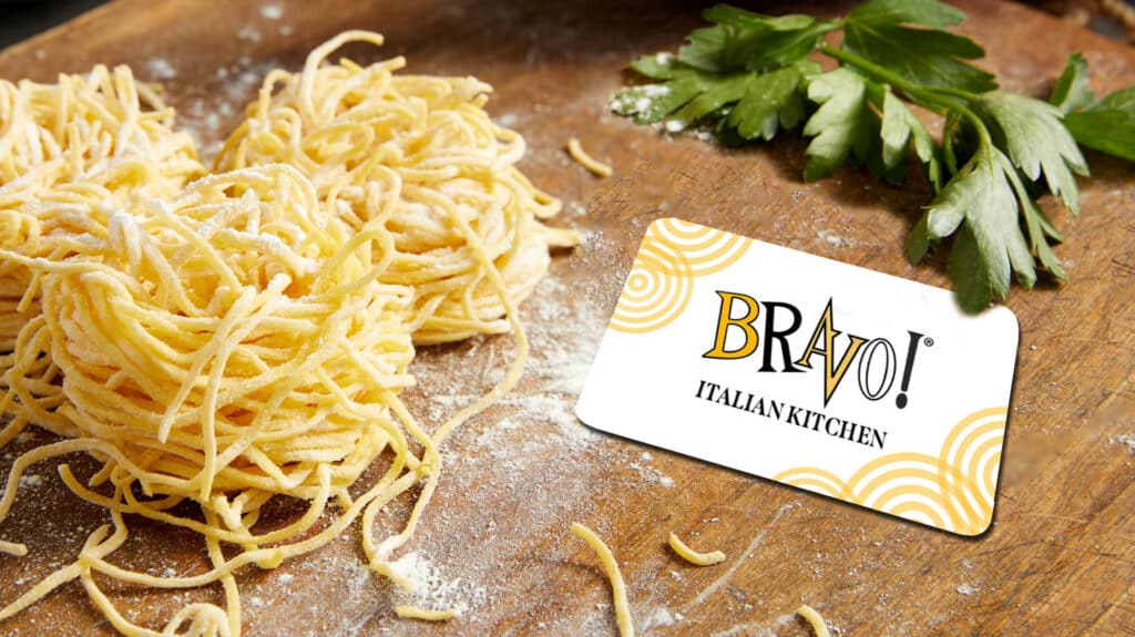 Fresh ingredients with pasta on a wooden board next to a Bravo Italian Kitchen Gift Card