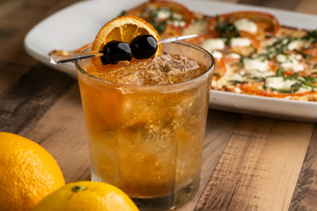 Orange cocktail garnished with cherries beside a flatbread.