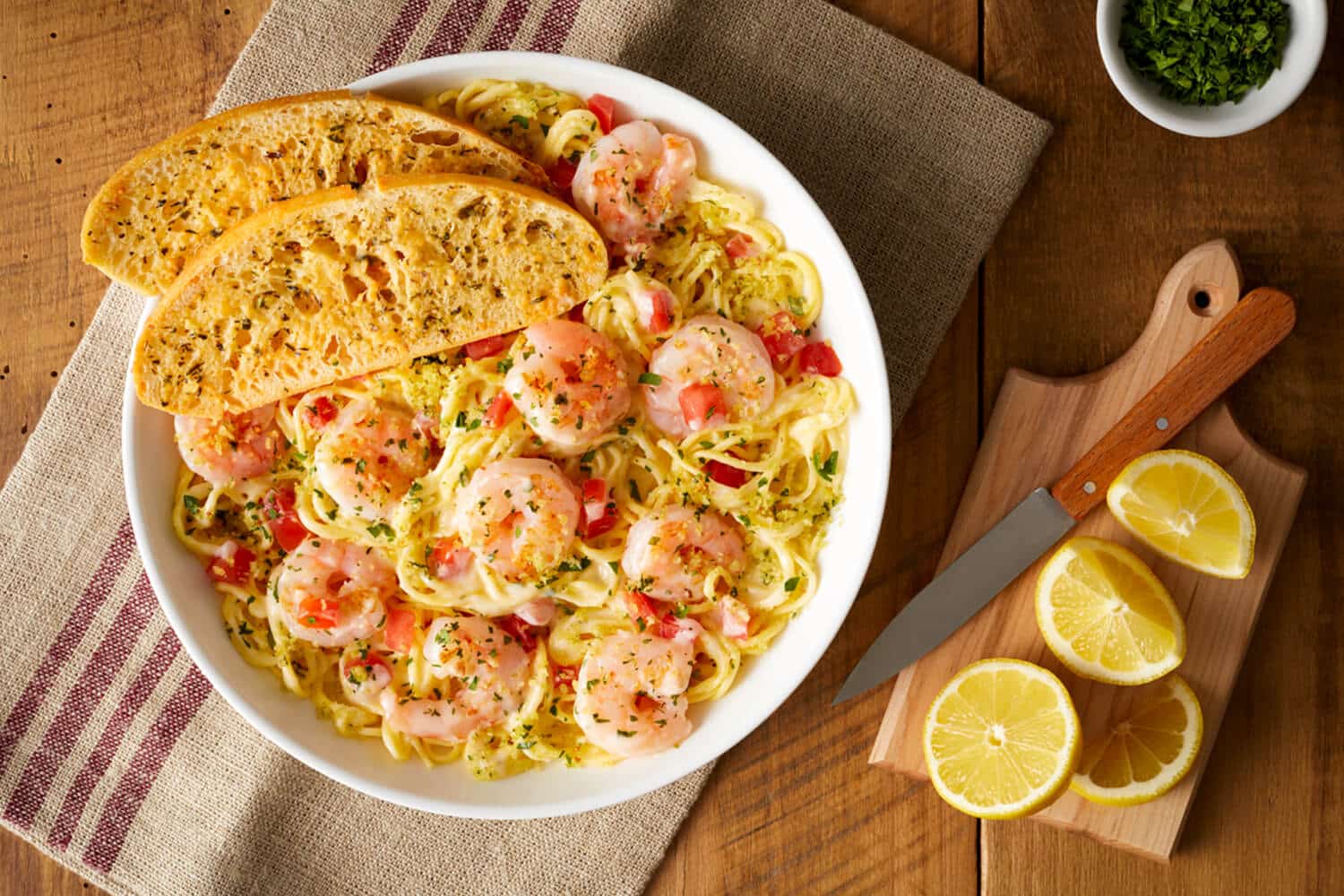 Shrimp Scampi plated with garlic bread and sliced lemons on the side from Bravo