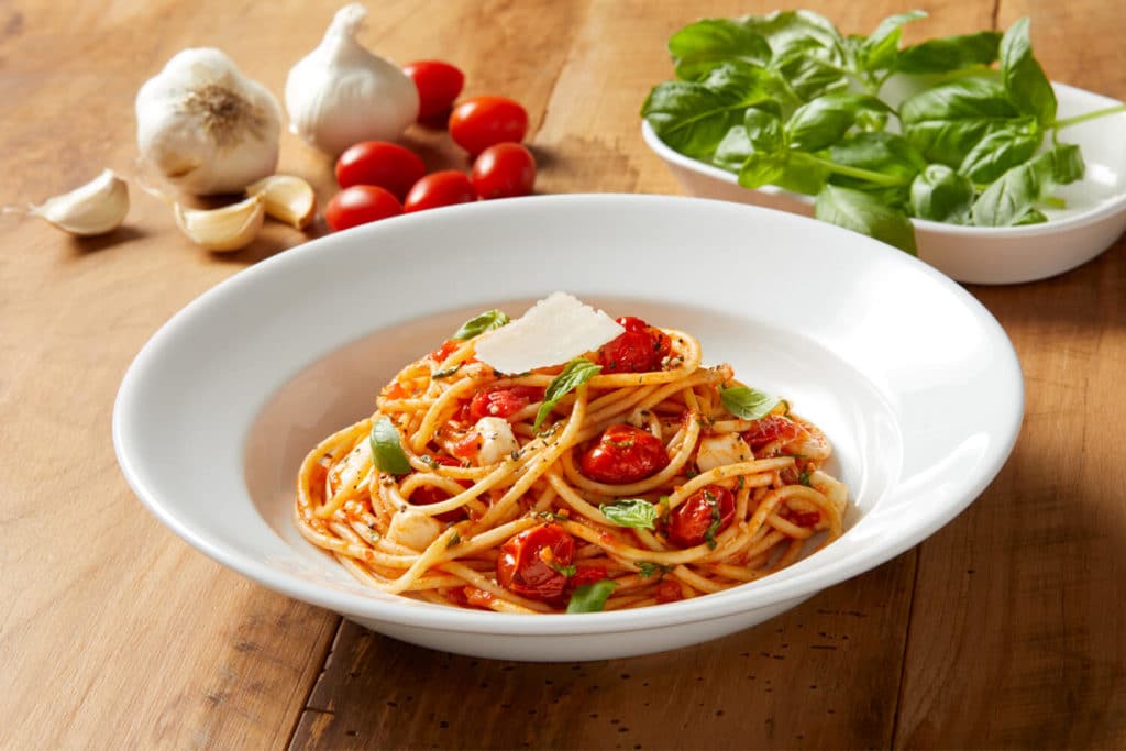 Spaghetti Pomodoro in a bowl from Bravo with fresh ingredients on wooden table