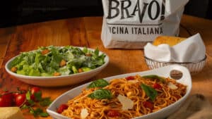 Bravo's spaghetti pomodoro and caesar salad on a wooden background with fresh tomatoes and parmesan