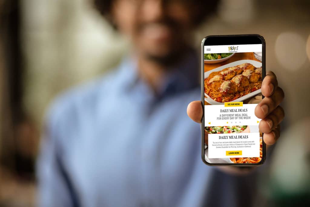 A photo of a man holding up a phone displaying the Bravo website
